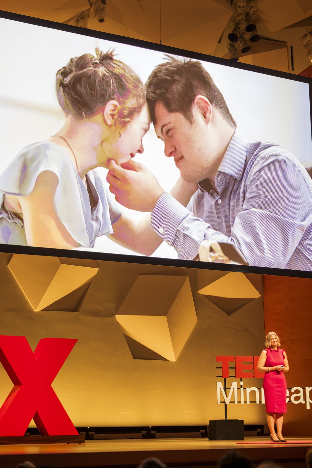 Katherine on stage as a photo of a couple fills the screen behind her