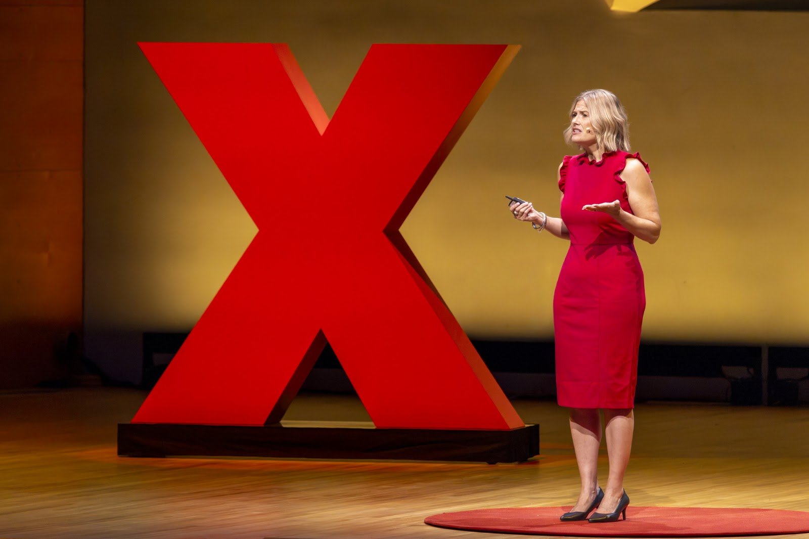 Katherine speaking beside the large red TEDx X on stage