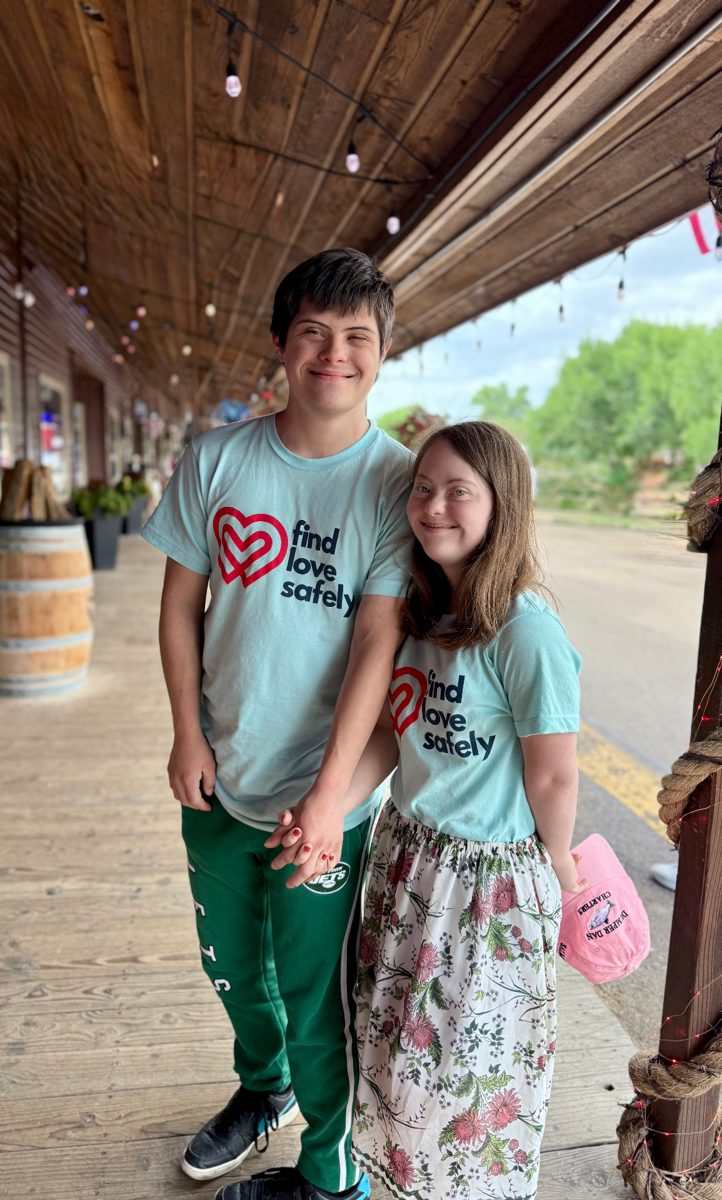 Nicolas and Stella holding hands in Find Love Safely shirts on a wooden boardwalk