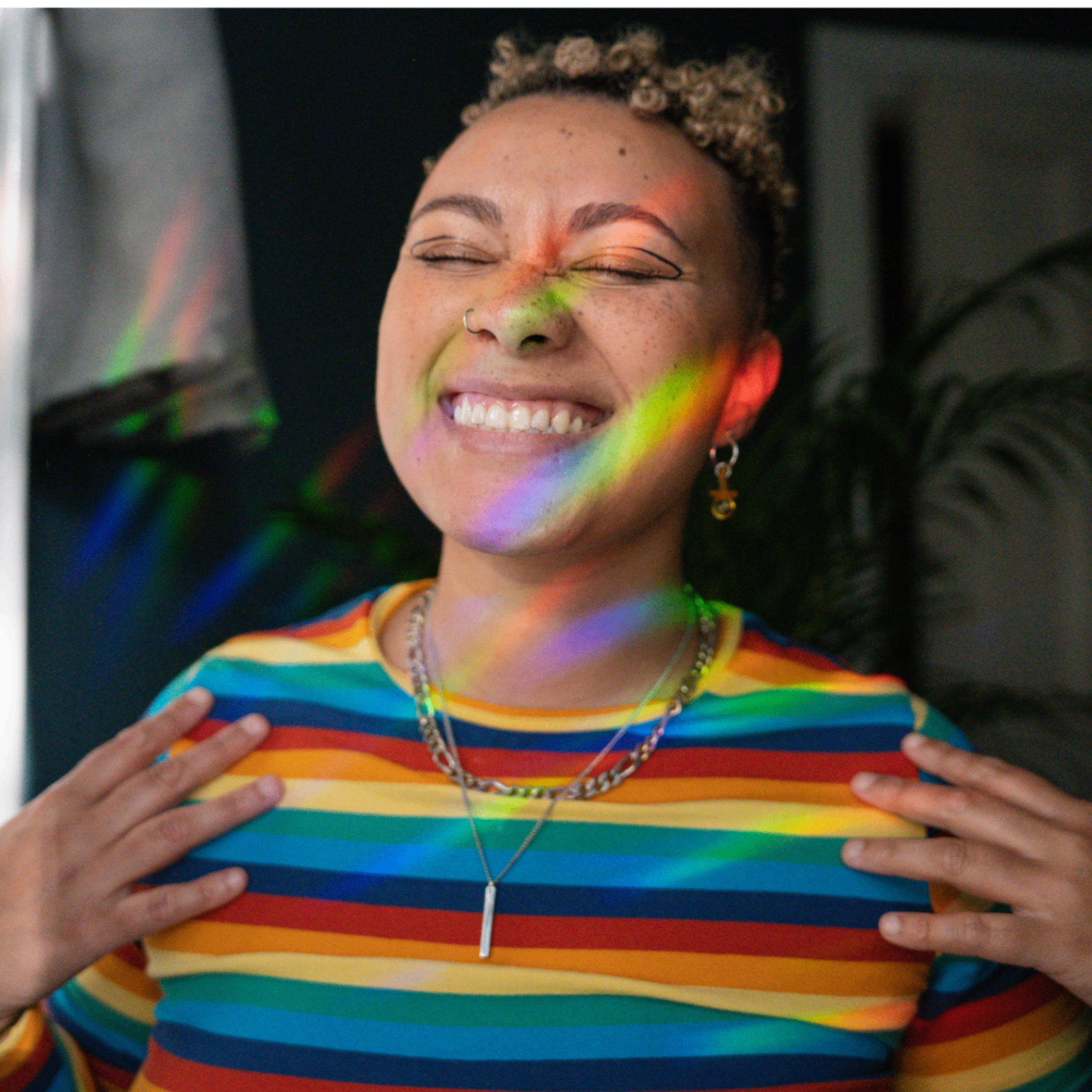 Smiling person in a rainbow striped shirt with light refracting across their face