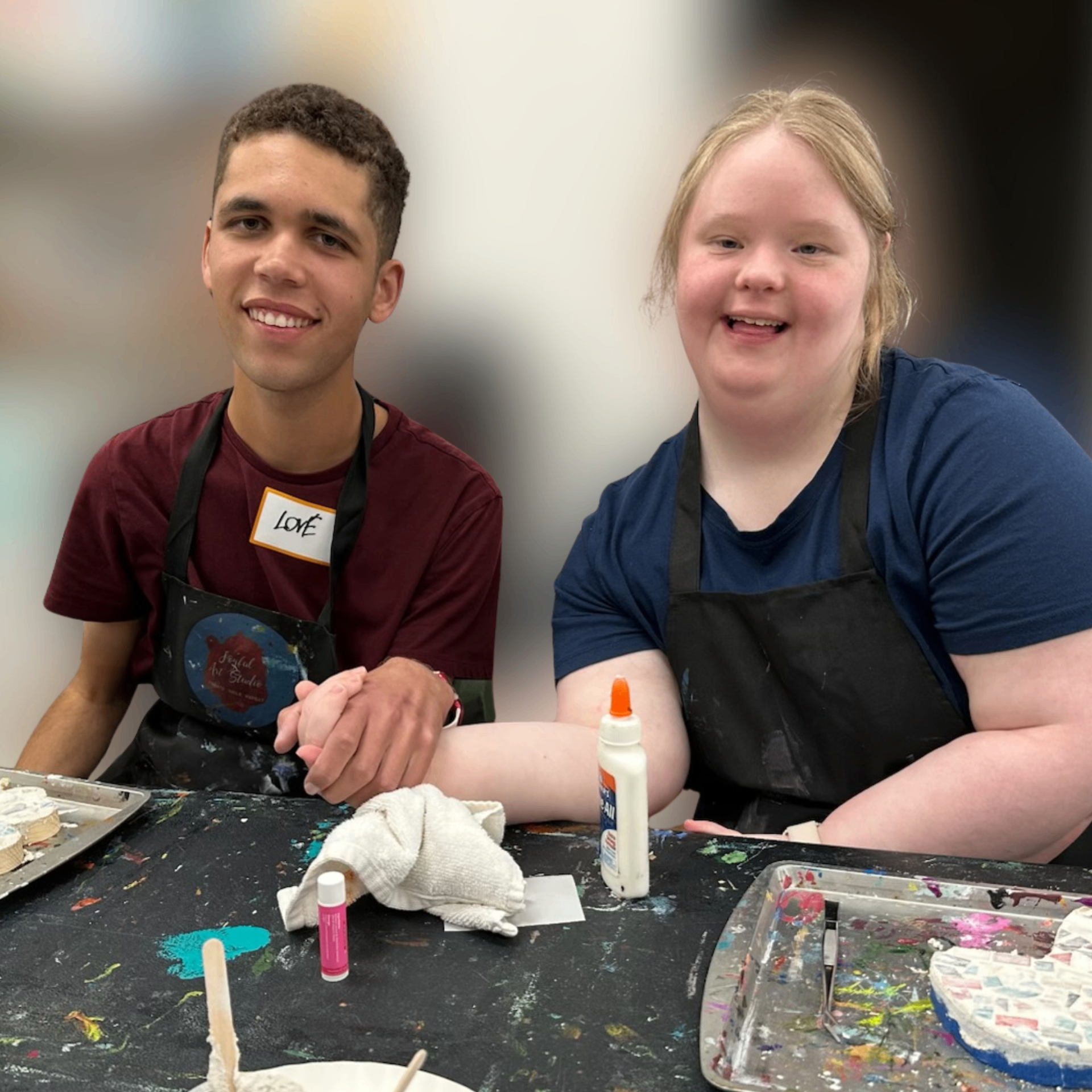 Two young adults with IDD smiling and holding hands