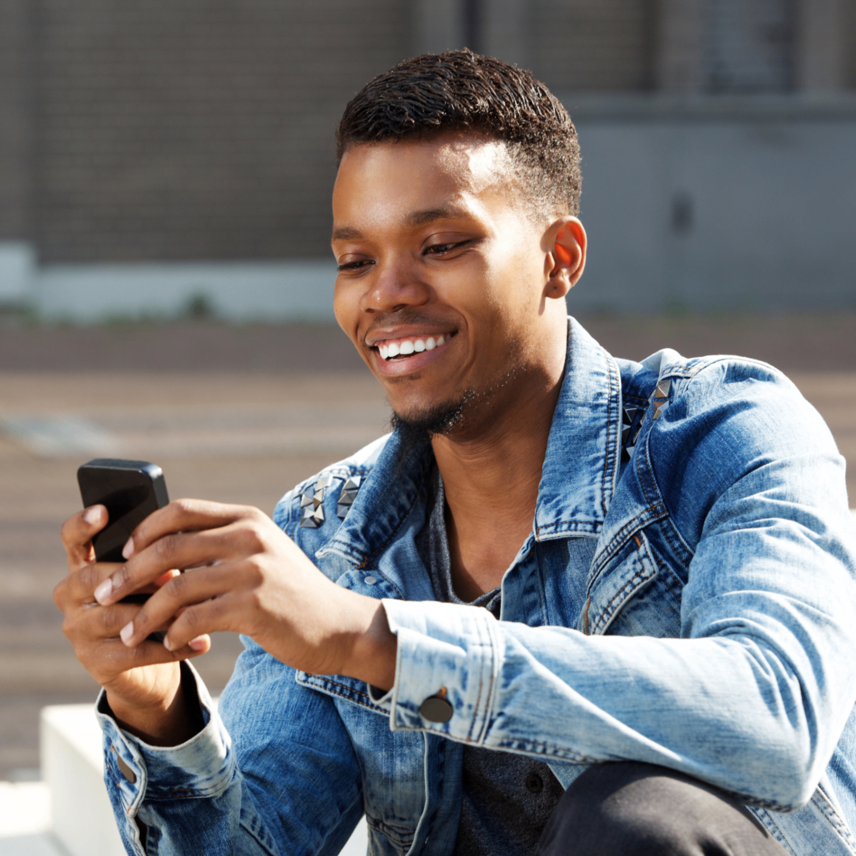 A smiling young man in a denim jacket looking at his phone